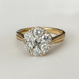 A Vintage Designer Iliana Diamond Cluster Ring. Sparkling diamonds claw set, 7 bright modern brilliant cut diamonds in a 'flowerhead' style. The centre diamond 0.5ct with 6 surrounding modern brilliant cut diamonds, in all totalling 2.7ct weight of diamonds. The yellow gold shank is marked 18k & 750 with a London Hallmark plus makers mark Illiana. The beautiful gallery has a pierced swirling design. 