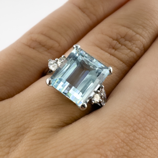Emerald Cut Aquamarine & Diamond Dress Ring. A striking aquamarine and diamond 1950's dress ring featuring a beautifully proportioned emerald-cut aquamarine displaying delicate sea-blue tones. The substantial centre stone is 6ct and is mounted in an 18ct white gold four-claw setting, framed by elegant diamond-set shoulders totalling 0.35ct. The gallery features beautiful scroll and pierced designs. Each shoulder is adorned with a combination of marquise-cut and round brilliant diamonds, creating a sophisticated balance of geometric and organic forms while adding additional brilliance to the design. The aquamarine measures 12mm x 10mm. The clean architectural lines of the emerald cut showcase the aquamarine's remarkable clarity, whilst the 18ct white gold setting enhances the gemstone's cool, watery hues. Elegant and dramatic in equal measure, this ring offers impressive finger coverage and makes a wonderful statement piece.  Please contact us if you would like to know more about this gorgeous ring or visit us at Saddingtons Jewellery, Mayfair.