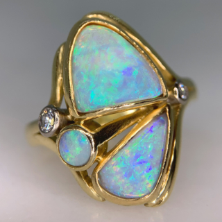 Fancy Asymmetric Water Opal and Diamond Ring in 18ct Yellow Gold, Hallmarked London, 1963. The unusual vintage custom made ring holds three vibrant water opals, two are of asymmetric shape, one circular. The opals are a mesmerising turquoise blue and purple with hints of green and yellow, we would even go as far as saying the colours are fluorescent. The split shoulders are decorated with two brilliant cut diamonds, of different cartage. The total head of the ring measures approximately 21.8 mm x 17 mm, The depth of the head 7 mm approximately. All the stones are bezel set in a half round polished shank. This ring is in immaculate condition, the opal will be professionally polished before any purchase. 