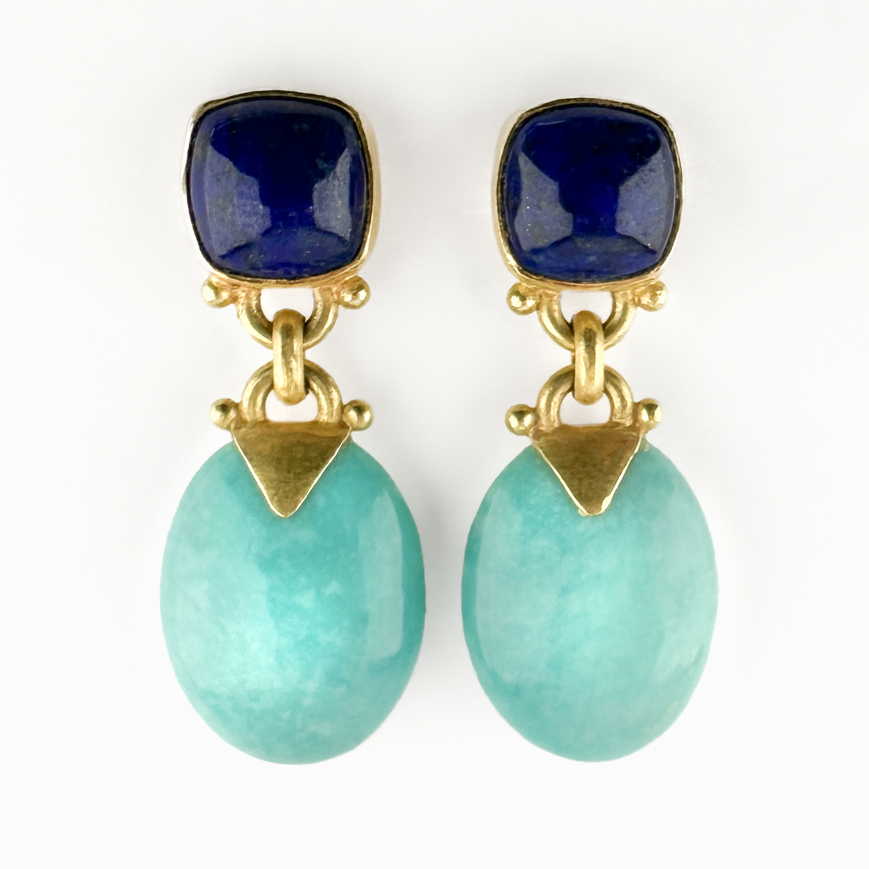 Lapis Lazuli & Turquoise Drop Earrings. A vibrant and beautifully balanced pair of vintage 18ct gold drop earrings, combining the rich cobalt-blue tones of lapis lazuli with vivid turquoise oval drops. The one of a kind craftsman made earrings are designed with cushion-shaped lapis lazuli studs suspending polished turquoise drops with articulated gold links that allow gentle movement when worn. The bold contrast creates a striking Mediterranean palette, while the clean geometric gold detailing lends the design a refined contemporary edge. Small triangular gold connectors introduce an architectural element and their compact proportions make them highly wearable while still offering a confident statement. The gold on the earrings has a matte finish. The drops measure 30mm with the lapis measuring 8.5x8.5mm and the turquoise 16x12mm. Please contact us if you would like to know more about these stunning earrings or visit us at Saddingtons Jewellery, Mayfair.