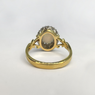 Vintage Vibrant White Opal Diamond Cluster Ring. Striking cabochon white oval opal with vibrant flashes of green and blue with a backdrop of pink glowing flashes. The opal is surrounded by a halo of eight cut natural mined diamonds.The head of the ring measures 1.3mm x1.1mm and sits low on the finger. The shank is beautifully scrolled in 18ct yellow gold and gem set in platinum. A stunning statement antique ring. Please contact us for further information on this ring.