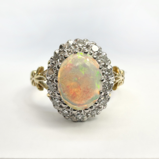 Vintage Vibrant White Opal Diamond Cluster Ring. Striking cabochon white oval opal with vibrant flashes of green and blue with a backdrop of pink glowing flashes. The opal is surrounded by a halo of eight cut natural mined diamonds.The head of the ring measures 1.3mm x1.1mm and sits low on the finger. The shank is beautifully scrolled in 18ct yellow gold and gem set in platinum. A stunning statement antique ring. Please contact us for further information on this ring.