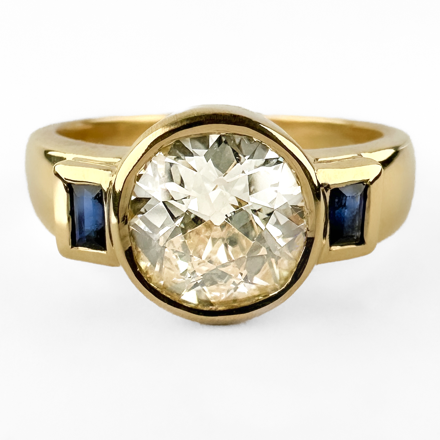 Excellent 1.63ct Diamond & Sapphire Ring. An amazing diamond and sapphire ring centred upon a magnificent Victorian old-cut diamond weighing approximately 1.63 carats, later mounted in an elegant contemporary 18ct gold setting. The beautifully proportioned diamond displays the broad, lively facets and distinctive character associated with Victorian-cut stones. Exhibiting a delicate light yellow tint, the diamond possesses exceptional presence and warmth, complemented by two baguette-cut sapphires set either side of the principal stone. The rich blue sapphires provide a sophisticated contrast to the diamond, creating a refined and timeless design. The contemporary 18ct gold mount has been thoughtfully designed to showcase the antique diamond while offering the durability and wearability expected of modern jewellery. The clean geometric lines of the setting allow the beauty of the historic stone to take centre stage. A wonderful marriage of antique and contemporary craftsmanship, this ring would make an exceptional engagement ring or a distinctive addition to any fine jewellery collection. Please contact us if you would like to know more about this brilliant stunning ring or visit us at Saddingtons Jewellery, Mayfair.