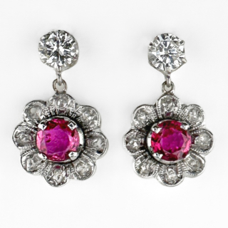 Pretty Drop Ruby & Diamond Flower Earrings. The earrings have a central 0.4ct deep pink ruby set in 18ct white gold and platinum. The ruby is encircled by 8 rose cut twinkling diamonds in a stylised flower drop with milgrain edging. The top of the earrings have a claw set brilliant cut diamond which has a bale where the flowerhead drops. The fitting is post and butterfly. The earrings drop 1.8cm from the top of the stud to the bottom of the flower. The drops give these elegant earrings a gentle sway when worn. Please contact us if you would like to know more about these beautiful earrings or visit us at Saddingtons Jewellery, Mayfair.
