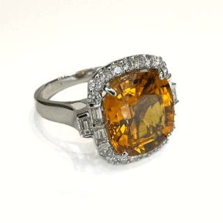 Beautiful Glowing 7ct Orange Yellow Sapphire Cluster Ring.Set in 18ct white gold with a large square cushion cut sapphire surrounded over 1ct of brilliant cut and emerald cut diamonds G-H colour and VS clarity.All stones are claw set except the 3 emerald cut diamonds on each side of the shoulders.The shank is marked 750 (18ct).Size M1/2 in UK sizing but can be resized.Please contact us if you would like further information on this stunning ring.