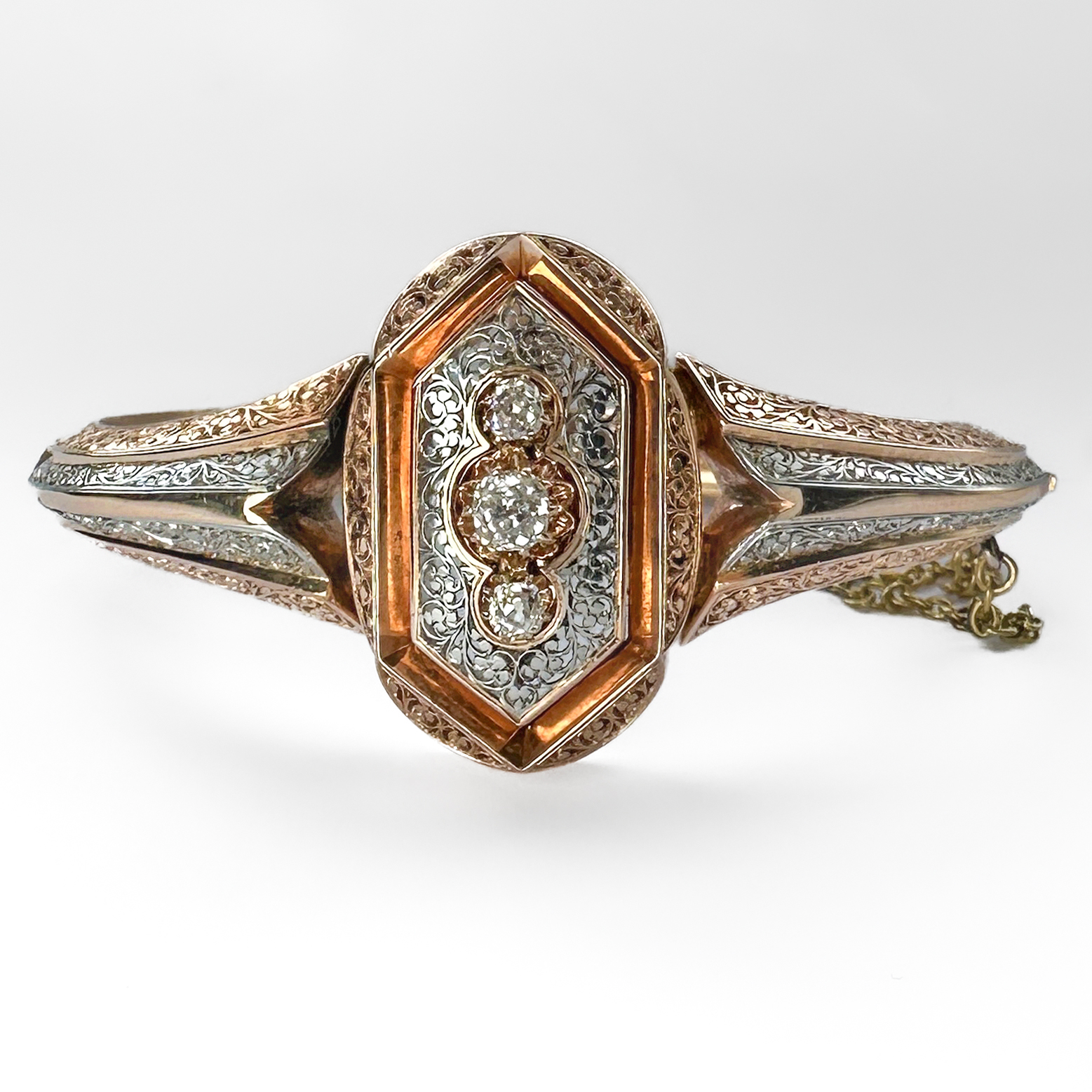 Unusual Antique Rose Gold & Platinum Diamond Bangle. This beautiful late Victorian/Edwardian bangle is made up of ribbed and pierced designed platinum and 18ct rose gold. The top half of the bangle is very finely pierced with scroll and berry design - this is a very fine piece of craftsmanship. The head if the bangle is set with 3 victorian cushion shaped brilliant cut diamonds, weighing a total of 0.60 cts. The bangle features 1900-1910 french 18ct import mark. The hinged tongue and box fastening features a yellow gold safety chain for security, this is very typical of late victorian bangles. Please contact us if you would like to know more about this bangle or visit us at Saddingtons Jewellery, Mayfair.