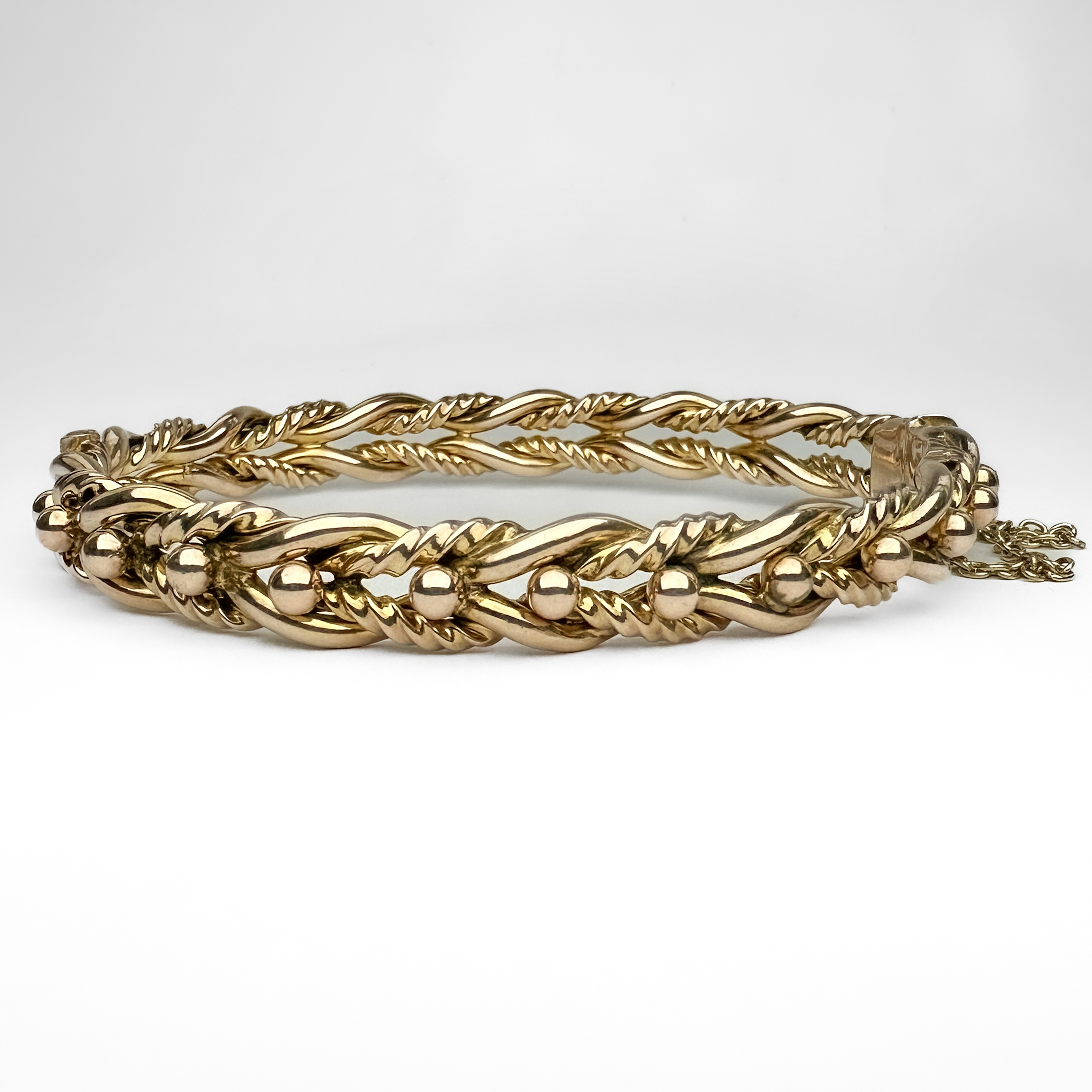 Pretty Edwardian Gold Bangle. This beautiful bangle has a knotted and ribbed wire design with a traditional bead decoration to the front half. The hinged tongue and box clasp has a safety chain for extra security. The bangle is made from 9ct stamped yellow gold and has a makers mark stamped in the inside. Please contact us if you would like to know more about this bangle or visit us at Saddingtons Jewellery, Mayfair.