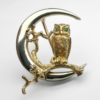 Vintage Gold Owl In The Moon Brooch. This sweet brooch depicts an owl on a branch in the crescent moon. It is made from 9ct white and yellow gold and has two emeralds for the eyes. On the back of the owl there is a 1987 Birmingham hallmark and a makers mark above. The brooch measures at 25mm in diameter and weighs 6.7 grams. Please contact us if you would like to know more about this beautiful brooch or visit us at Saddingtons Jewellery, Mayfair.