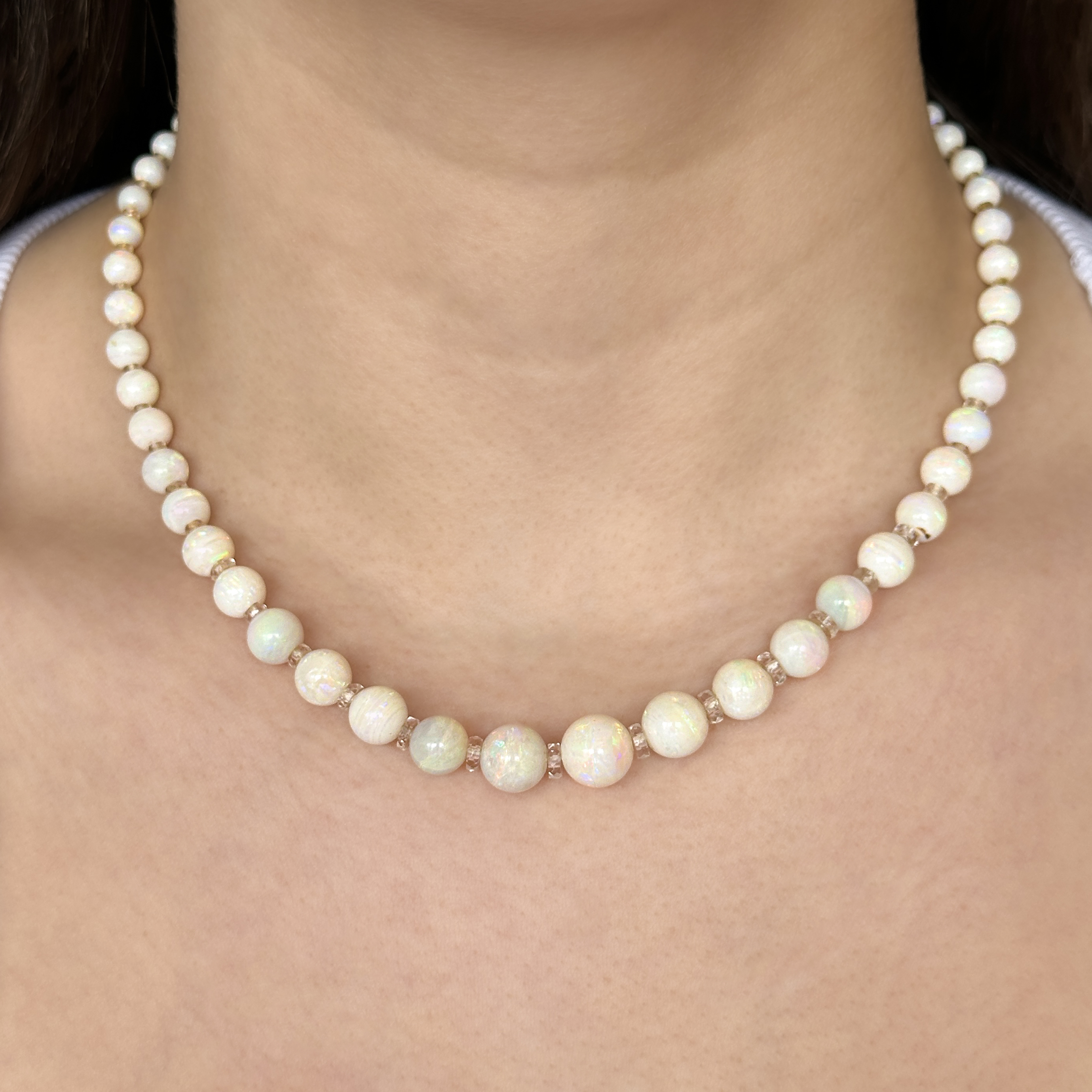 Pretty Edwardian Opal Beaded Necklace. This beautiful graduated spherical opal bead necklace features 60 white opals with rock crystal roundel spacers, except from the last 2 inches on either side. The necklace measures 17 inches. The biggest opal measures 10.3mm and the smallest is 3.8mm. The white gold clasp has 13 small diamonds set into it and also features a makers mark. Please contact us if you would like to know more about this necklace or visit at Saddingtons Jewellery, Mayfair.