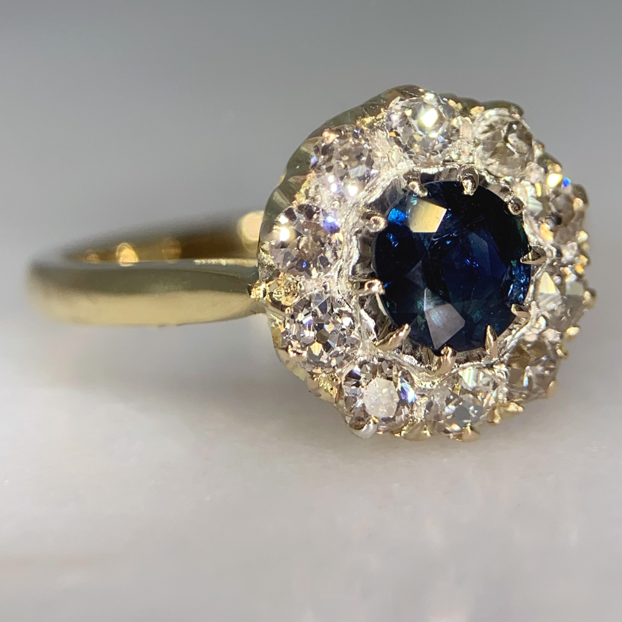 Stunning Circular Sapphire and Diamond Halo Cluster Ring in tested 18ct Yellow Gold. The ring has an unmarked smooth polished split shoulder shank. The basket and head diameter measures approximately 11.5 mm, with a depth of 6.5 mm. The central sapphire is a mesmerising deep blue and measures approximately 5.8 mm in diameter. The sapphire is encapsulated by 10 old cut diamonds, all stones are claw set. The ring is in immaculate condition.