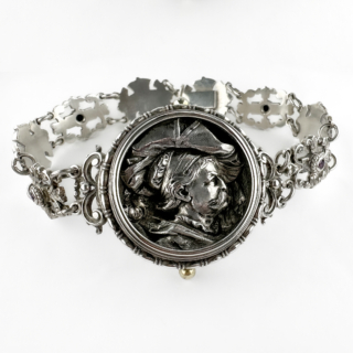 Sophisticated Georg Adam Scheid Art Nouveau Silver Bracelet. An exceptional Art Nouveau silver and garnet bracelet by renowned Austrian designer Georg Adam Scheid, circa 1880, with G A S hallmark on the back. Crafted in richly detailed silver, the bracelet is formed from alternating openwork links combining flowing scrollwork with bold sculptural face motifs, accented throughout with deep red garnets. At the centre sits a dramatic high-relief portrait medallion depicting a Renaissance-style gentleman in a broad plumed hat, rendered with remarkable sculptural depth and expression. The medallion possesses the character of a miniature Renaissance portrait plaque, giving the bracelet an unusually artistic presence. The design beautifully reflects the artistic experimentation of the Austrian Vienna Secession and Neo-Renaissance Art Nouveau movement, where jewellery often blended mythology, historic revivalism and sculptural craftsmanship into highly individual wearable works of art. The oxidised silver finish enhances the depth and architectural quality of the bracelet, while the garnets add warmth and contrast against the cool silver tones. The bracelet features a hidden box clasp fastening. Bold, unusual and highly collectable, this bracelet wears as both a historic artistic object and a striking contemporary statement piece. The bracelet measures at 19.8cm long, the central piece has a diameter of 3.2cm. Please contact us if you would like to know more about this wonderful bracelet or visit us at Saddingtons Jewellery, Mayfair.