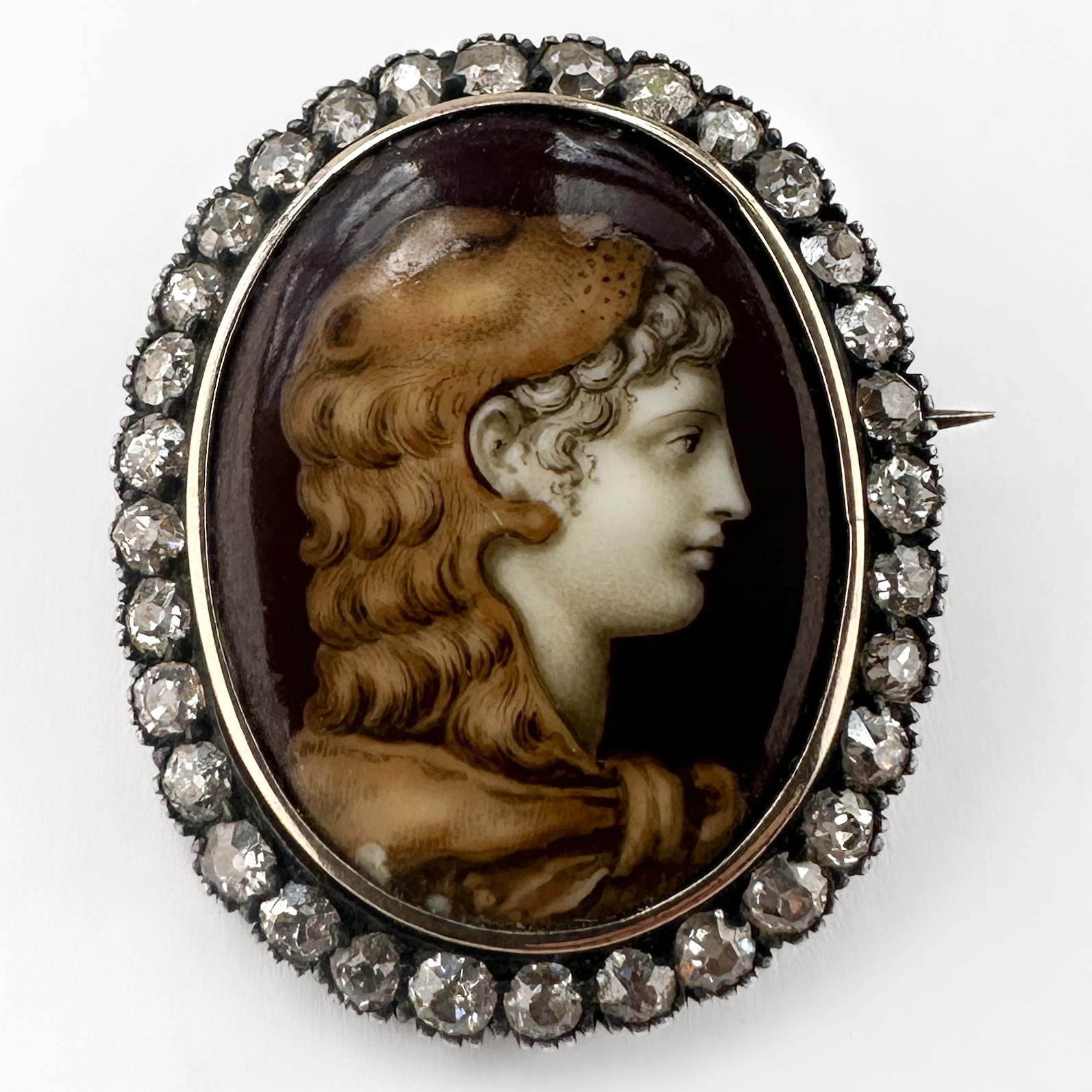 Victorian Diamond & Enamel Hercules Portrait Brooch. An exceptional antique late Victorian classical portrait brooch, centred with an enamel plaque depicting a heroic Greco-Roman male profile traditionally identified as Hercules. Rendered in rich sepia and ivory tones, the finely detailed portrait displays strong Neo-Classical influence, inspired by ancient Roman and Grand Tour artistic traditions so admired during the 19th century. The oval portrait plaque is framed by a glittering border of 33 old-cut diamonds, totalling to 1ct in a silver-topped gold setting, creating beautiful contrast and soft antique brilliance. The brooch measures 2.8cm x 2.2cm. Pieces of this nature were often collected as expressions of education, travel and appreciation for antiquity. This piece comes in the box pictured. Please contact us if you would like to know more about this wonderful brooch or visit us at Saddingtons Jewellery, Mayfair.