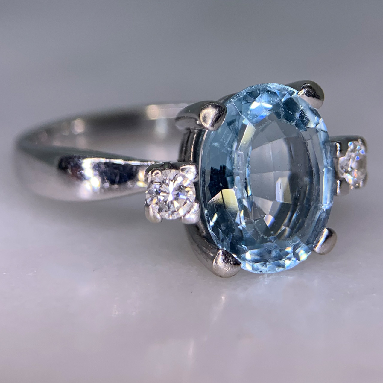 Exquisite Outsized Aquamarine and Diamond Trilogy Ring, in stamped 18ct White Gold. The centre aquamarine measures 3.8carats, enclosed by two diamonds. All the stones are claw set and measure 16 mm x 12 mm together, with a basket depth of 7 mm. The ring has a stylish flat-sided court shank, with a sort of square outer appearance. Excellent ring.