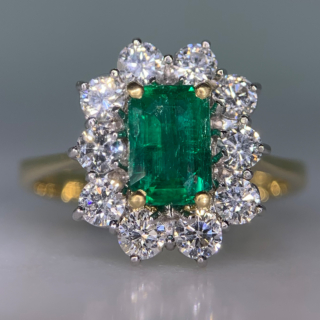 Outstanding Emerald and Diamond Rectangular Cluster Ring in 18ct Yellow Gold, Hallmarked London, 1990. The exquisite ring has a 1.4carat immaculate glowing emerald as a centre stone, surrounded by 1.02carats of brilliant cut, bright white diamonds (total diamond weight). All the stones are claw set in a platinum basket, with a reverse taper, raised flat band shank. The head of the ring measures approximately 14 mm x 12.5 mm. The ring is in absolutely immaculate condition.