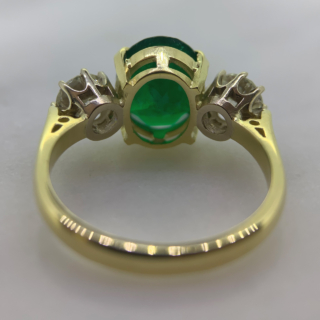 Exquisite Emerald and Diamond Trilogy Ring, in 18ct hallmarked yellow Gold, Birmingham 1996.  The centre deep emerald measures  11 mm x 9 mm and is enclosed by two diamonds totalling at 1.10carats of diamond weight. The total ring head measures 20 mm in width. All the stones are claw set with a basket depth of 6mm. The shank is polished with tiffany shoulders.  Excellent ring.