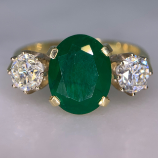 Exquisite Emerald and Diamond Trilogy Ring, in 18ct hallmarked yellow Gold, Birmingham 1996.  The centre deep emerald measures  11 mm x 9 mm and is enclosed by two diamonds totalling at 1.10carats of diamond weight. The total ring head measures 20 mm in width. All the stones are claw set with a basket depth of 6mm. The shank is polished with tiffany shoulders.  Excellent ring.