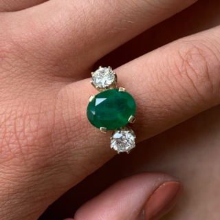 Exquisite Emerald and Diamond Trilogy Ring, in 18ct hallmarked yellow Gold, Birmingham 1996.  The centre deep emerald measures  11 mm x 9 mm and is enclosed by two diamonds totalling at 1.10carats of diamond weight. The total ring head measures 20 mm in width. All the stones are claw set with a basket depth of 6mm. The shank is polished with tiffany shoulders.  Excellent ring.