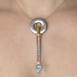 Completely Unique Jewellery Art Work From Designer Tom Rucker Satellite Platinum and Aquamarine Brooch/Pendant. The almost sculpture like brooch/pendant is designed by hand by master and award winning jewellery designer Tom Rucker. The design is long and slim 10cm long, 3.2cm wide at the top of the brooch/pendant. The top, a frosted platinum circle, dropping to a cylindrical cage tube with aquamarines within. The end of the piece has an arrow shaped rub over set aquamarine. The mesmerising piece has an overall appearance of a stylised space rocket or satellite in a futuristic arrow design. A centerpiece. There are 2 rows of square brilliant diamonds set one each at each end, set in 18ct yellow gold. The back of the piece, the 2 pronged pin with a catch to secure. Additionally, at the back of the circle there is an integral fitting for a chain. We show this piece with a wire 18ct yellow chain which is available to purchase with our piece, (not included). Futuristic and statement. Please contact us if you would like to know more about this stunning piece or visit us at Saddingtons Jewellery, Mayfair.