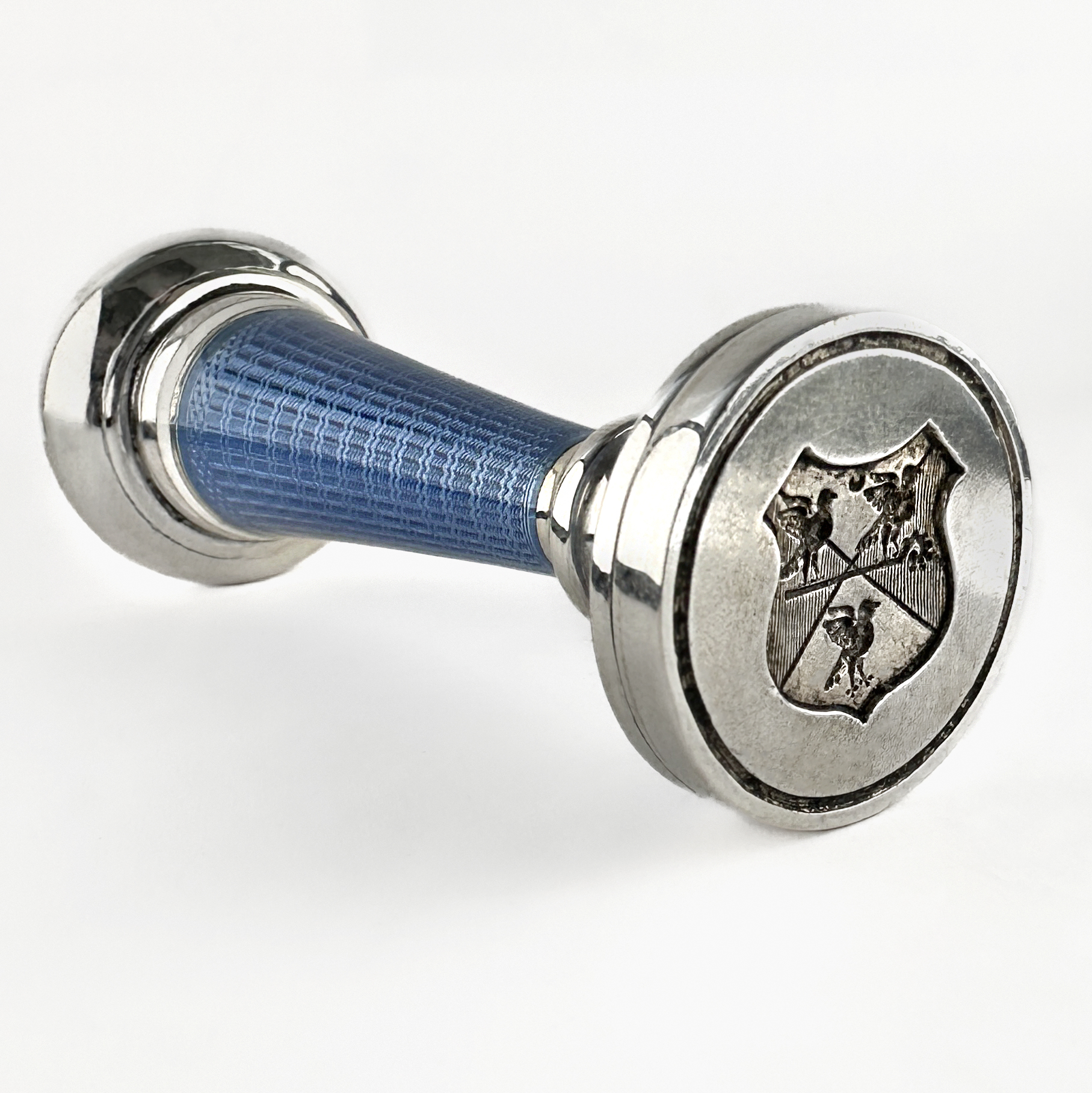 Wonderful Guilloché Enamel Desk Seal With Heraldic Crest Intaglio. A refined antique Edwardian guilloché enamel desk seal, crafted in silver with an engraved heraldic crest intaglio matrix. The elegant baluster-shaped handle is decorated with beautifully preserved powder-blue guilloché enamel, laid over fine engine-turned engraving that catches and reflects the light with exceptional delicacy. The silver mounts provide crisp contrast to the translucent enamel and enhance the sophisticated architectural form of the seal. The base is engraved with an heraldic shield featuring stylised birds and armorial detailing, intended for use with sealing wax on personal correspondence and official documents. Such desk seals were prized symbols of refinement and status during the late 19th and early 20th centuries. The whole piece is 6.8cm long with the stamps diameter measuring 2.5cm. Please contact us if you would like to know more about this brilliant antique or visit us at Saddingtons Jewellery, Mayfair.