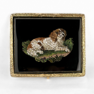 Victorian Dog Mosaic Brooch. An exceptional antique Victorian micro mosaic brooch crafted in 18ct gold, dating from the mid to late 19th century. The rectangular plaque is finely decorated with an exquisitely detailed micro mosaic depicting a reclining King Charles spaniel-type dog within a naturalistic landscape. Executed using incredibly small hand-set glass tesserae, the mosaic displays remarkable precision and artistry, particularly in the intricate rendering of the dog’s fur and surrounding foliage. Set against a rich black ground, the colourful mosaic composition is framed within an elegant nicely engraved 18ct gold mount that enhances the refinement of the piece without detracting from the extraordinary craftsmanship. Micro mosaic jewellery of this quality was highly sought after during the Victorian Grand Tour period, when affluent travellers acquired finely worked Roman mosaics as sophisticated souvenirs and collectors’ pieces. Animal subjects, particularly dogs, were especially admired for their symbolism of loyalty and companionship. The brooch measures 4x4.7cm. Please contact us if you would like to know more about this wonderful brooch or visit us at Saddingtons Jewellery, Mayfair.