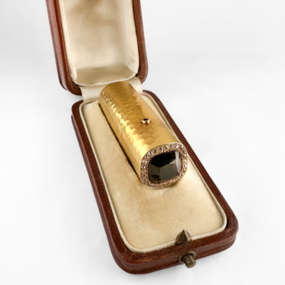 Excellent Edwardian Garnet & Diamond Scent Bottle. An exceptional antique Edwardian scent bottle crafted in 15ct gold. The cylindrical body is finished with a beautifully hand-hammered surface, reflecting the refined craftsmanship and Arts & Crafts influence of the period. The hinged lid is centred with a richly coloured cushion-shaped warm cognac-toned hessonite garnet surrounded by a delicate border of sparkling brilliant cut Edwardian diamonds, creating elegant contrast against the warm gold tones. Opening the garnet spring loaded push piece to reveal its original scent compartment and internal stopper, the piece was designed as a luxurious personal scent bottle for perfume or aromatic essences. The piece measures 5.5x1.7cm and comes in its original box. Functional objects of this quality were treasured vanity accessories during the Edwardian era, combining practicality with sophisticated goldsmithing. Please contact us if you would like to know more about this fantastic antique or visit us at Saddingtons Jewellery, Mayfair.