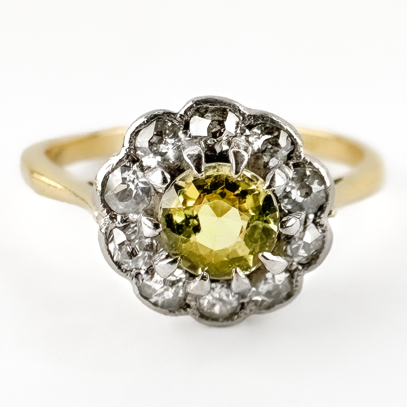 Edwardian Yellow Sapphire & Diamond Cluster Ring. A charming Edwardian ring featuring a natural yellow sapphire weighing 0.3cts and 0.3cts total of Edwardian cut diamonds. The cluster is mounted in platinum, whilst the elegant shank is crafted in 18ct yellow gold, a classic combination favoured during the Edwardian era. On the shank there is a plat and an 18ct stamp. The yellow sapphire displays an attractive golden-buttery hue, beautifully complemented by the bright old-cut diamonds that encircle it. The delicate scalloped platinum setting creates a floral-inspired cluster design, reflecting the refined and feminine aesthetic for which Edwardian jewellery is celebrated. Combining exceptional craftsmanship with timeless elegance, this antique ring is a wonderful example of early 20th-century design. Whether chosen as a unique engagement ring or added to a fine jewellery collection, it offers both rarity and enduring appeal. Please contact us if you would like to know more about this gorgeous ring or visit us at Saddingtons Jewellery, Mayfair.