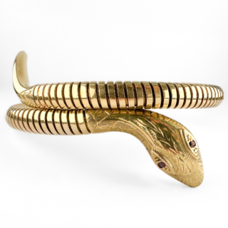 Vintage Snake Bangle. This striking vintage snake bangle is crafted in 9ct yellow gold and bears Birmingham hallmarks for 1986. Designed as a coiled serpent wrapping elegantly around the wrist, the bangle features beautifully engraved detailing to the head and scales, with faceted ruby eyes providing a flash of colour. The snake motif has long been associated with eternal love, wisdom and protection, making serpent jewellery one of the most enduring and collectible designs in jewellery history. Popularised during the Victorian era and remaining highly sought after today, snake jewellery continues to captivate collectors with its symbolism and distinctive appearance. The flexible coiled design allows the bangle to sit comfortably on the wrist, while the richly coloured gold and engraved decoration highlight the quality of its craftsmanship. The ruby-set eyes add a subtle but luxurious finishing touch, bringing life and character to the piece. Please contact us if you would like to know more about this lovely snake bangle or visit us at Saddingtons Jewellery, Mayfair.