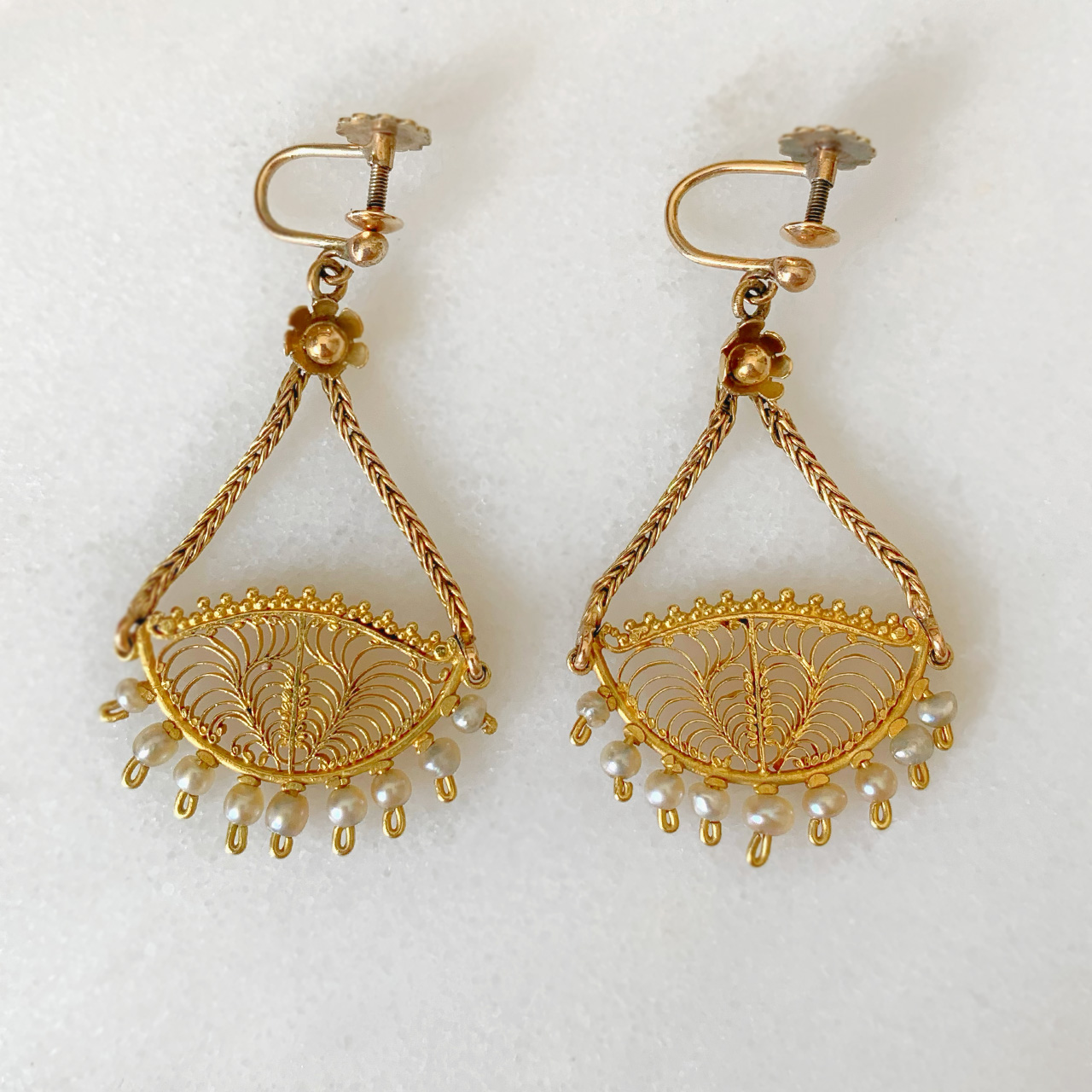 Incredible Pearl and Filigree Chandelier Earrings, in stamped 9ct Yellow Gold. Each earring holds 9 natural pearls, below an intricate filigree design. The design measures 25 mm in width and hangs beautifully by two foxtail chains that meet at a daisy design flower. The total earring design measures 43 mm x 25 mm. The earrings have a screw back fitting for non pierced ears, however can be worn by both pierced and non-pierced.