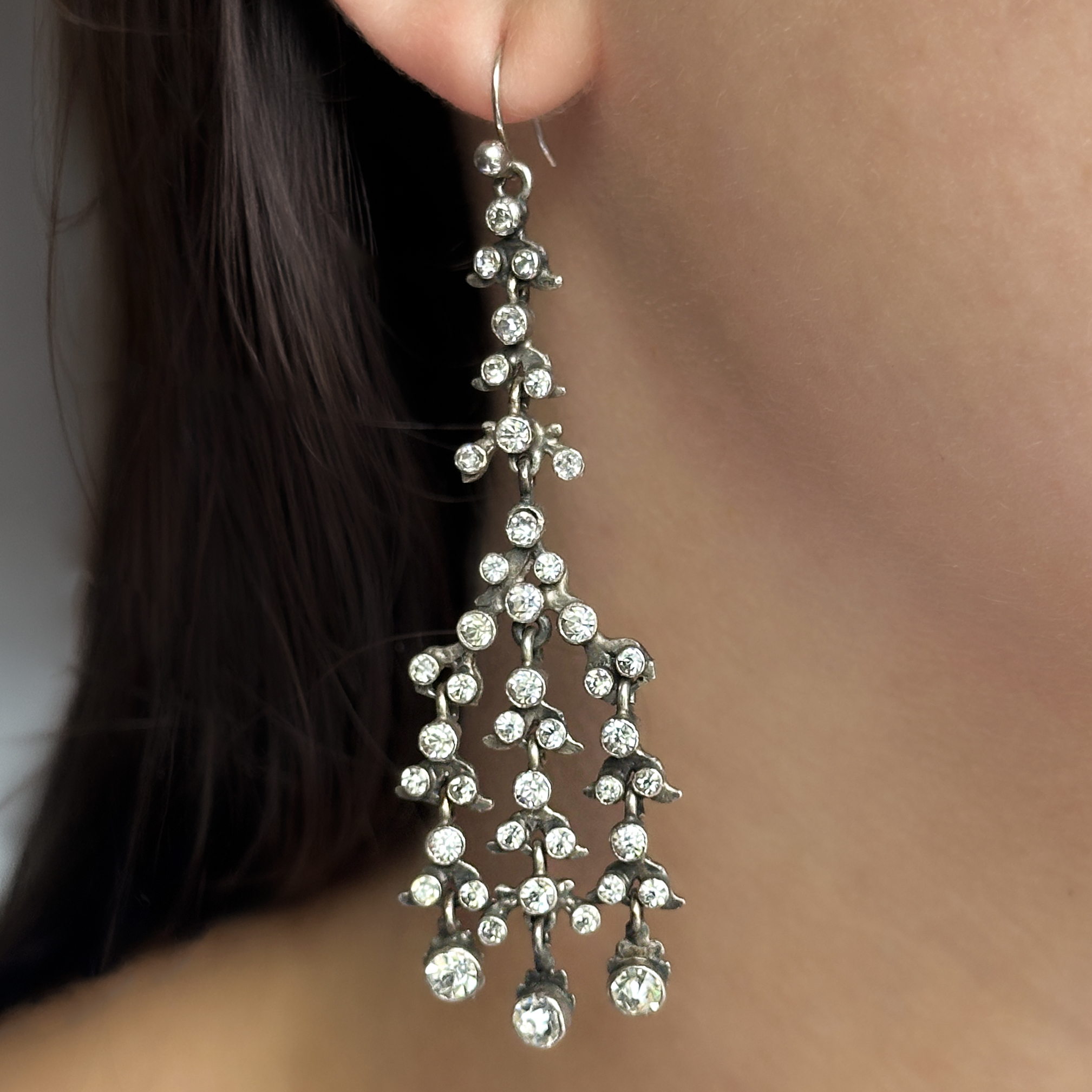 Edwardian Paste Chandelier Earrings. An elegant pair of Edwardian paste chandelier earrings, beautifully crafted in silver and set throughout with sparkling graduated paste stones. Designed to imitate the brilliance of diamonds, these finely made earrings capture the refined glamour and sophistication of the Edwardian era. They measure from top to bottom of drop 6.2cm. The earrings are formed as delicate cascading branches adorned with numerous individually set paste stones, creating exceptional movement and sparkle when worn. Their graceful chandelier design reflects the light beautifully, whilst the intricate openwork construction gives them a wonderfully light and feminine appearance.  During the Edwardian period, high-quality paste jewellery was highly fashionable and often worn alongside fine jewellery at society events. Today, original Edwardian paste earrings are treasured for their craftsmanship, elegance and remarkable sparkle. These earrings comes boxed. Please contact us if you would like to know more about these gorgeous earrings or visit us at Saddingtons Jewellery, Mayfair.