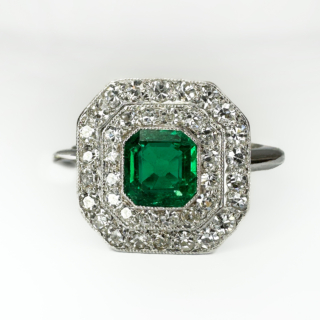 A beautiful Art Deco Emerald & Diamond Cluster Ring.This beautifully handmade ring is set with a central emerald which is approximately 4.8mm x 5mm,surrounded by 2 rows of transitional cut diamonds,the measurement of the head of the ring is 12 x 12mm.The diamonds are pave set and edged milgrain.The underside of the mount has a pierced ribbon gallery,the mount and shank are in platinum (marked in the shank).This is a superb and original antique ring.The ring sits comfortable and low on the finger.Please contact us if you would like to know more about this ring.