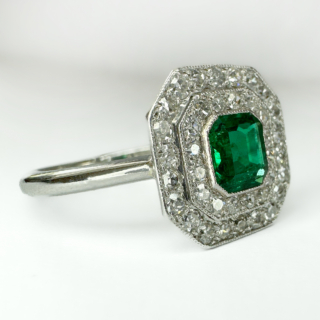 A beautiful Antique Emerald & Diamond Cluster Ring.This beautifully handmade ring is set with a central emerald which is approximately 4.8mm x 5mm,surrounded by 2 rows of Edwardian diamonds,the measurement of the head of the ring is 12 x 12mm.The diamonds are pave set and edged milgrain.The underside of the mount has a pierced ribbon gallery,the mount and shank are in platinum (marked in the shank).This is a superb and original antique ring.The ring sits comfortable and low on the finger.Please contact us if you would like to know more about this ring.