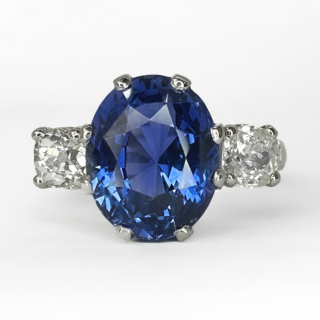 Stunning Natural No Heat 7.47ct Ceylon Sapphire Trilogy Ring. This beautiful antique  ring has one large faceted oval velvety blue sapphire. The sapphire has a gemmological certification (GCS), the sapphire measures 11.69 x 9.35 x 7.78mm. The ring has a transitional brilliant cut diamond either side of the central stone. All gems are claw set. The mount is platinum and this is engraved inside the ring shank. The ring can be resized, please contact us if you would like to know more about this ring or visit us at Saddingtons Jewellery, Mayfair.