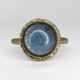Dainty Antique Moonstone Ring. A beautiful cabochon single stone blue gray moonstone measuring 0.8cm, the whole head of the ring including the ring mount measures 1.0cm. The moonstone is rub over set with millegraine edging typical of the era. The back of the ring/cabochon is closed setting in gold. The ring sits flat and comfortable on the finger.