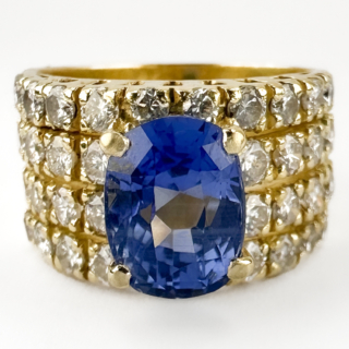 Stunning Ceylon Sapphire & Pavé Diamond Cocktail Ring. This amazing ring features a central natural unheated Ceylon sapphire that is claw set amongst a carpet of 36 pavé set natural diamonds. The total diamond weight is 0.9cts and they are round brilliant cut. The 2.58ct weighed sapphire is a stunning cornflower, mid blue shade. The 18ct yellow gold 4 band design creates a chunky and interesting wide band that is very comfortable on. The gallery features lattice style open work. On the back of the ring there is a 750 stamp. Please contact us if you would like to know more about this beautiful ring or visit us at Saddingtons Jewellery, Mayfair.