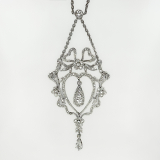 Stunning Antique Belle Epoque Diamond Heart Pendant. Edwardian Belle Epoque platinum and diamond heart and bow pendant, a beautiful example of Edwardian craftsmanship.  The chain and pendant are in platinum with the chain length 16 inches with the exquisite and ornate pendant dropping from the central rub over diamond by 2.5 inches. The body of the pendant has diamond set bows and flowers decorating the central heart which has an articulated pear shaped drop inside with a further smaller pear drop diamond from the bottom of the heart. Please contact us if you would like to know more about this rare pendant.