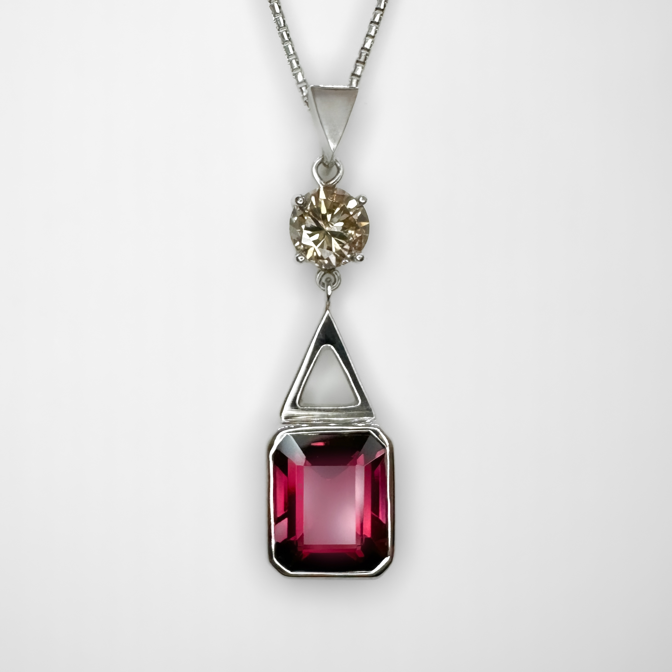 Striking Deep Pink Tourmaline Diamond Drop Pendant. A beautiful rectangular deep pink tourmaline set,measuring 12 x 10mm in 18ct white gold. The tourmaline has a 1.08ct brilliant cut diamond in a light fancy yellow. A unique and beautiful combination of gem colours. Above the diamond there is a robust triangular bale, the drop pendant measures 1.6 inches from the top of the bale to the bottom of the pendant. The pendant has a 15 inch 18ct white gold, hallmarked. The chain has a bolt ring fastening clasp.