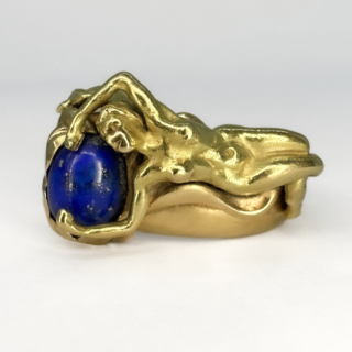 Styled Figurative Art Nouveau Lapis Lazuli Ring. A beautiful glowing 18ct yellow gold naked lady lying backwards over a lapis lazuli 'pillow'. This ring is a vintage  Art Nouveau style ring, the ring has a designers mark on the shank of the ring. The are carved scrolls and waves of gold around the lady, the ring design has a scroll open back. Please contact us if you would like to know more about this ring or come and visit at Saddingtons Jewellery, Mayfair.