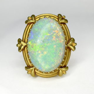 Arts and Crafts Opal Ring. This impressive ring features a bright oval opal that has brilliant play of colours and measures 20mm x 14mm, the stone sits in a 18ct yellow gold shank. This unusual and beautiful shank is well designed and an example of the designs in the arts and crafts movement. The top of the ring measures at 26mm x 22mm and sits comfortably on the finger. Please contact us if you would like to know more about this ring or visit us at Saddingtons Jewellery, Mayfair.