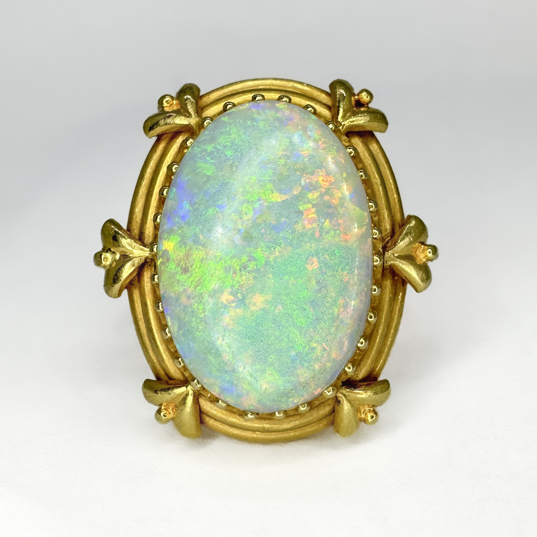 Arts and Crafts Opal Ring. This impressive ring features a bright oval opal that has brilliant play of colours and measures 20mm x 14mm, the stone sits in a 18ct yellow gold shank. This unusual and beautiful shank is well designed and an example of the designs in the arts and crafts movement. The top of the ring measures at 26mm x 22mm and sits comfortably on the finger. Please contact us if you would like to know more about this ring or visit us at Saddingtons Jewellery, Mayfair.