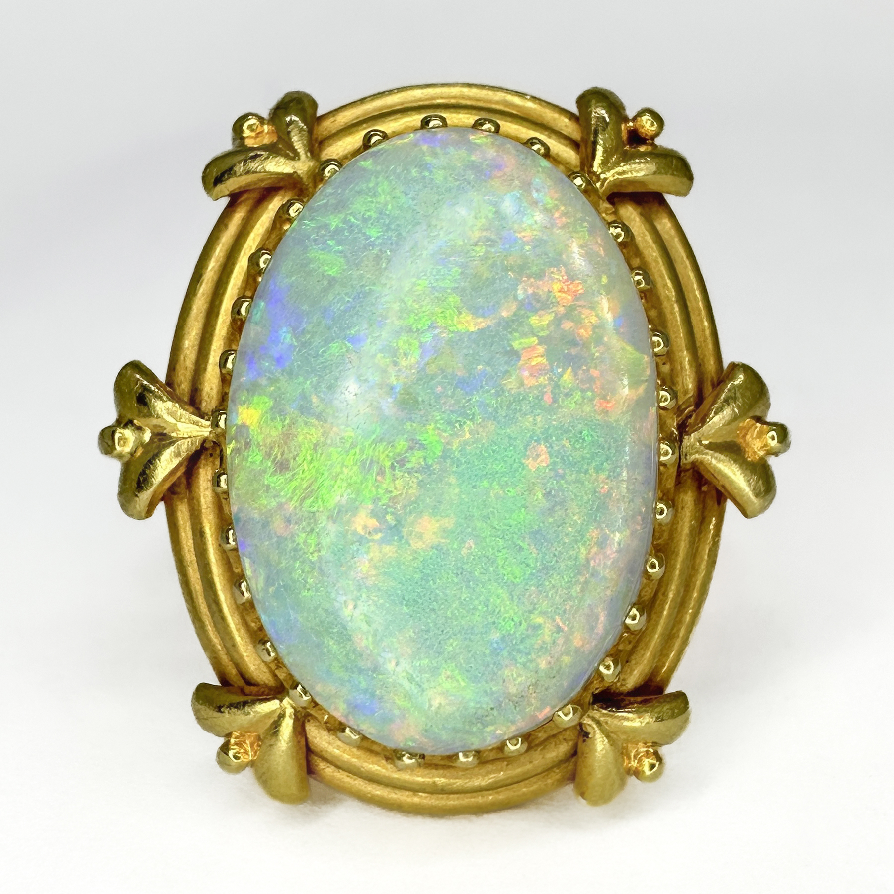 Arts and Crafts Opal Ring. This impressive ring features a bright oval opal that has brilliant play of colours and measures 20mm x 14mm, the stone sits in a 18ct yellow gold shank. This unusual and beautiful shank is well designed and an example of the designs in the arts and crafts movement. The top of the ring measures at 26mm x 22mm and sits comfortably on the finger. Please contact us if you would like to know more about this ring or visit us at Saddingtons Jewellery, Mayfair.