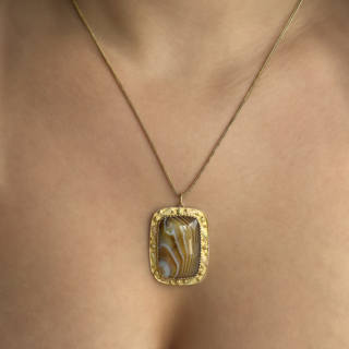 Beautiful Victorian Banded Agate Pendant With Chain. Elegant Victorian banded agate pendant set within an ornate 15ct gold mount and suspended from a fine 9ct gold chain. The striking natural agate panel displays beautiful natural banding in rich chocolate brown, caramel and smoky blue-grey tones, with delicate white striations creating a wonderfully atmospheric layered effect. The stone is framed by an intricately worked 15ct gold tricolour border decorated with fine floral and foliate engraving, adding warmth and refinement to the piece. Scottish agate jewellery became immensely fashionable during the Victorian period following Queen Victoria’s admiration for hardstone jewellery, and pieces displaying unusual colour combinations such as these soft blue and brown tones are especially sought after today. The total piece weighs 11.6g. The chain is 20.5inches long and commensurate with age although in great working order. The pendant is 3.7 x 2.7cm. Please contact us if you would like to know more about this stunning necklace or visit us at Saddingtons Jewellery, Mayfair.