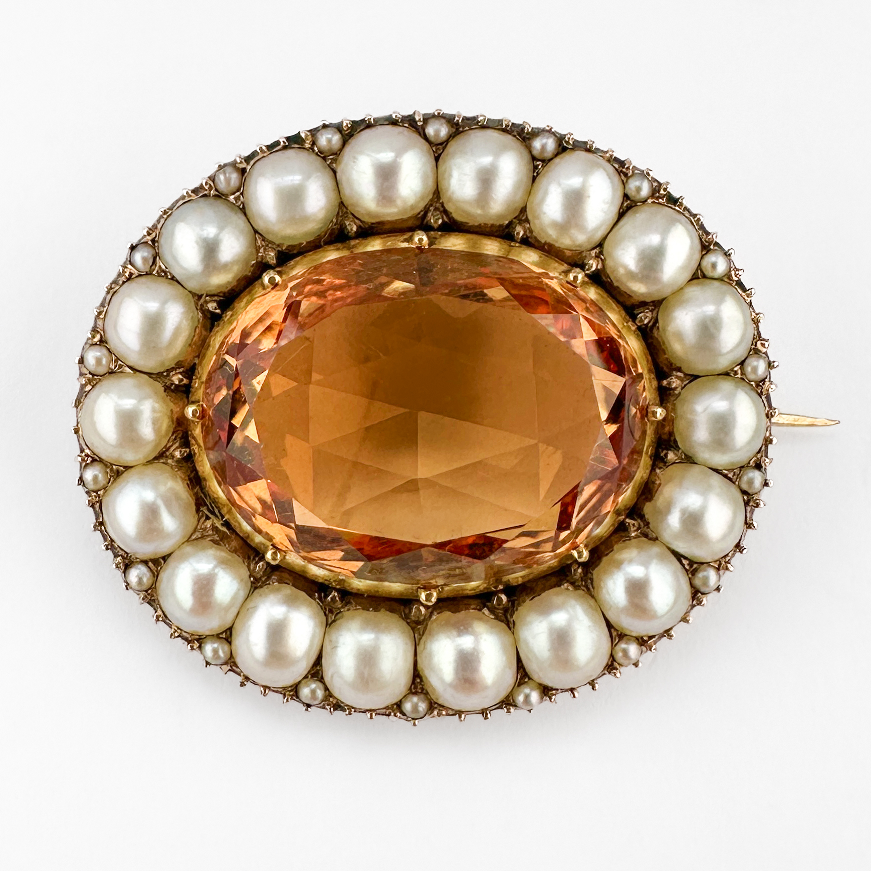 Stunning Victorian Topaz & Pearl Oval Brooch. Elegant Victorian topaz and natural pearl brooch set in rich 15ct gold. Centred with a large oval golden yellow topaz, the stone is surrounded by a beautiful border of luminous 1/2 pearls, with smaller pearls set as points between the larger pearls creating a classic Victorian cluster design full of warmth and refinement. The pearls are well matched and in beautiful condition. The richly toned stone displays deep honey and orange flashes which contrast beautifully against the soft glow of the pearls. Its generous scale and timeless design make it an exceptionally wearable antique statement brooch today. The central topaz measures 19 x 14mm and is 13cts. The brooch measures at 3 x 2.6 cm. The original back pin is shaped so the brooch doesn't tilt or fall when worn which is very typical of victorian design. The brooch comes in the boxed that it is pictured in. Please contact us if you would like to know more about this amazing brooch or visit us at Saddingtons Jewellery, Mayfair.