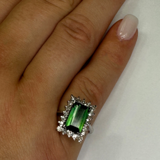 Green Tourmaline and Diamond Cluster Ring, a glorious transparent intense green rectangular tourmaline is surrounded by 20 round faceted diamonds. The diamond total weight 0.40cts. The central rectangular tourmaline measures 10.4mm long, 6.3mm wide and 3.8mm deep. The ring is claw set and has an 18ct (stamped) white gold shank, cradle set which is a typical design from 1960's. The ring sits comfortable and looks well on the finger. This ring can be resized.  Contact us if you would like further information or chat about this ring. 