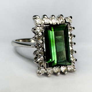 Green Tourmaline and Diamond Cluster Ring, a glorious transparent intense green rectangular tourmaline is surrounded by 20 round faceted diamonds. The diamond total weight 0.40cts. The central rectangular tourmaline measures 10.4mm long, 6.3mm wide and 3.8mm deep. The ring is claw set and has an 18ct (stamped) white gold shank, cradle set which is a typical design from 1960's. The ring sits comfortable and looks well on the finger. This ring can be resized.  Contact us if you would like further information or chat about this ring. 