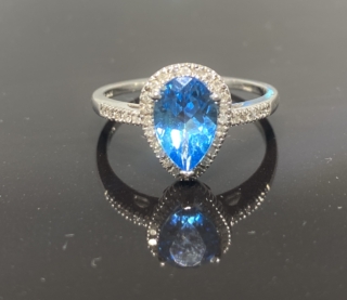 Blue Topaz Diamond Halo Ring, central pear shaped topaz surrounded with a halo of pave diamonds. The ring is in 10 ct white gold. The shoulders are set with pave diamonds also