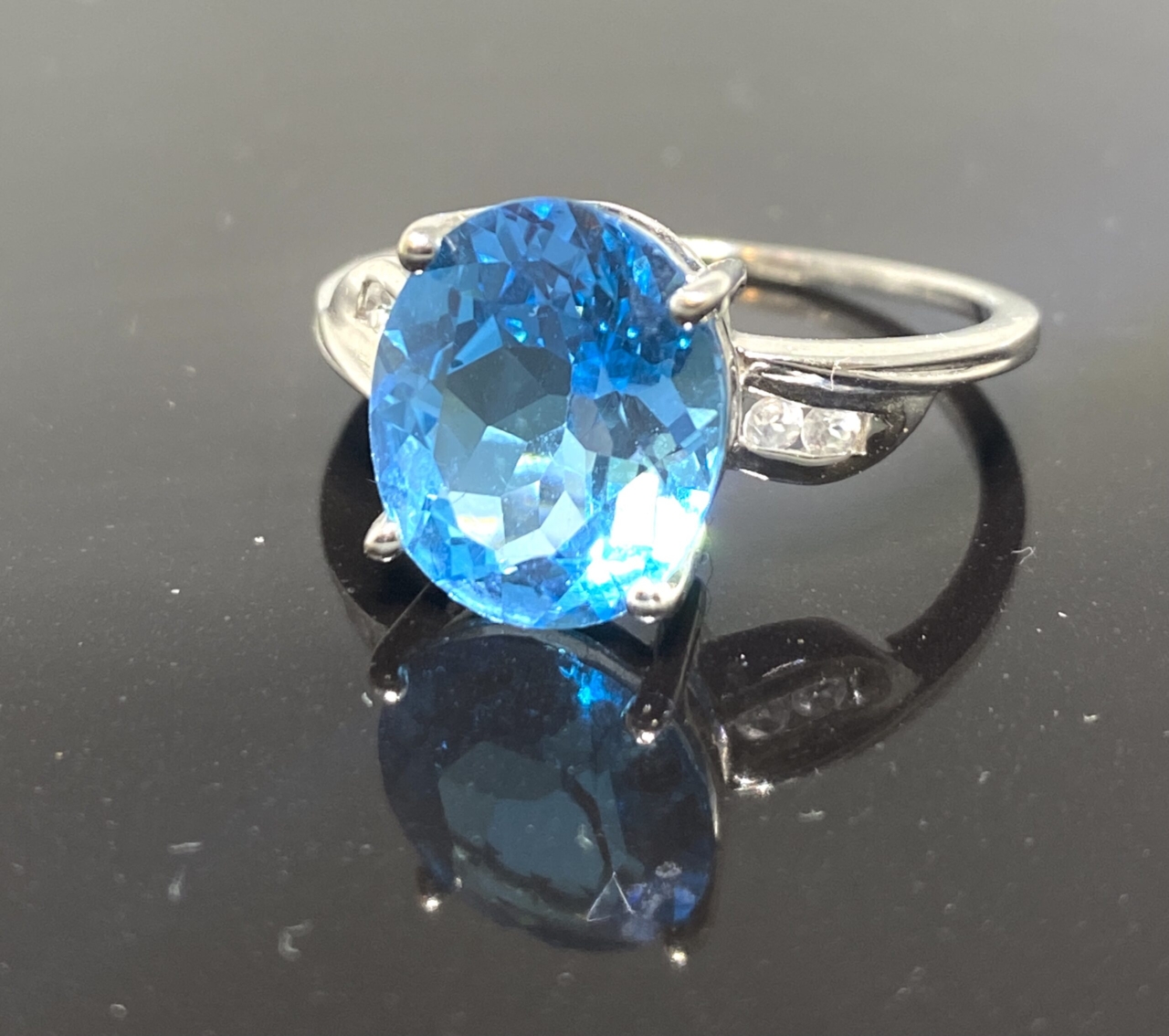 Blue Topaz & Diamond Ring in 9 ct white gold. The central mid blue faceted topaz is claw set, there are two small brilliant cut diamonds set in each side of the shoulders.