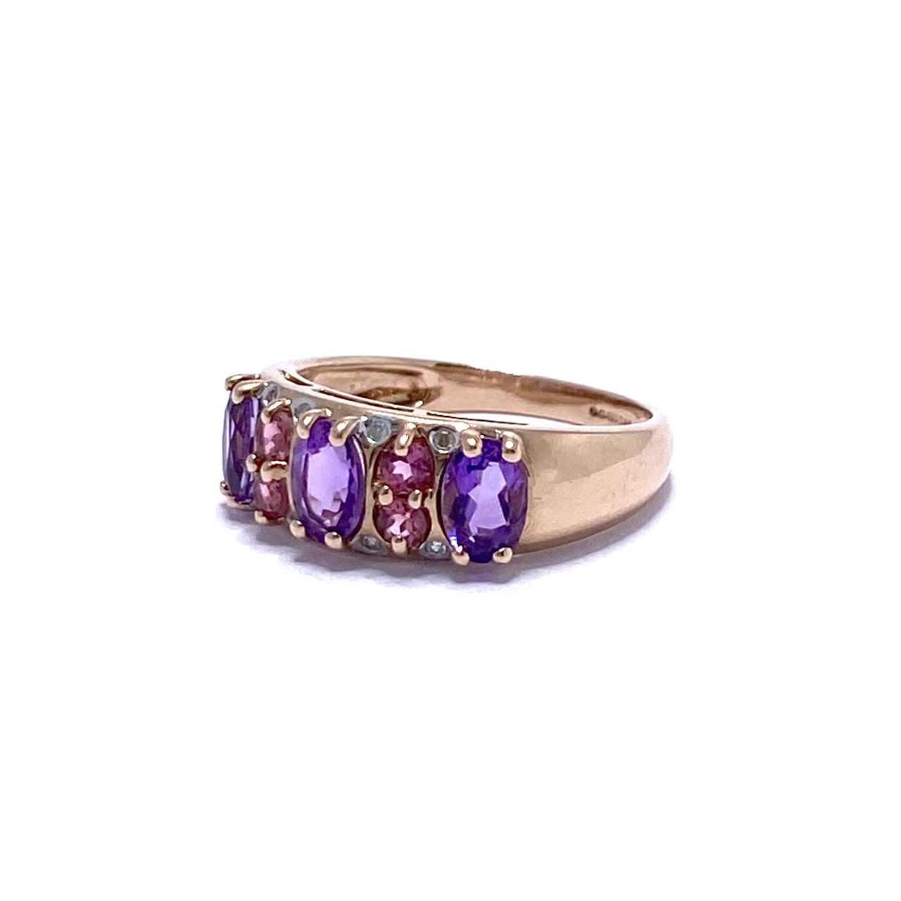 A 9ct Rose Gold Ring that tapers from front to back. It holds 3 light purple amethysts and four smaller vibrant pink amethysts. Lining the top and bottom of the front face are 8 micro diamonds.