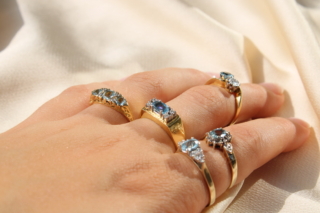 A left hand with 5 Aquamarine and Diamond vintage gold rings interspersed on the fingers.