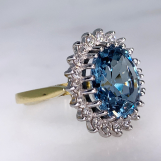 Aquamarine and Diamond Cluster Ring, 18ct Gold Hallmarked. The principle faceted Aquamarine and surrounding diamonds are claw set in a tiffany shank. The head of the ring measures approximately 18mm x 21mm.