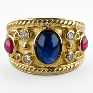 Wonderful Etruscan Cabochon Ruby & Sapphire Ring. A beautifully set rub over cabochon sapphire sits in the centre with 2 diamonds as accents and a stunning red round ruby on either side. The design is heavily influenced by classical Etruscan gold work, with intricate granulated detailing in the shank and scroll and rope sculptural forms that makes the ring look exceptional on the finger. The shank features an 18ct stamp alongside a GS makers mark and a continental assay mark. Likely of Swiss/Italian origin, circa 1970s–1980s, this is a beautifully made piece that reflects the high standard of continental gold-smithing of the period. Please contact us if you would like to know more about this incredible ring or visit us at Saddingtons Jewellery, Mayfair.